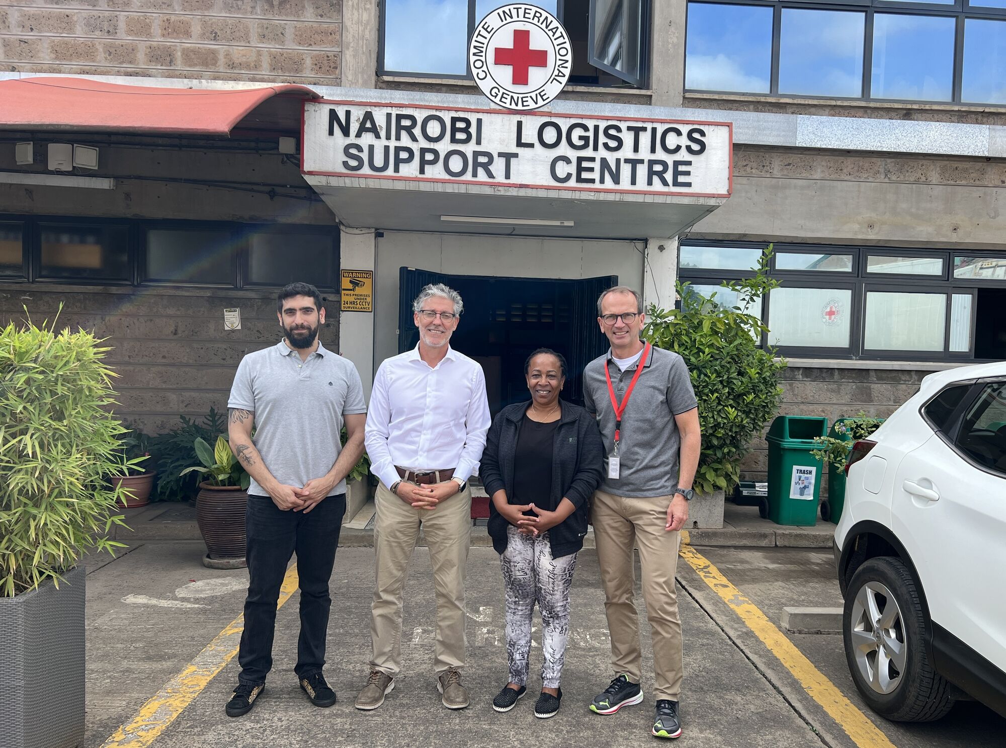 Prof. Wagner and Red Cross members standing in front of a building with a large red cross sign reading "Nairobi Logistics Support Centre"